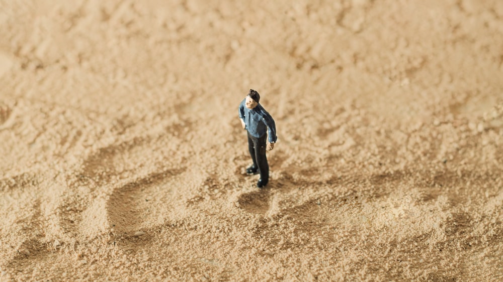 a miniature man standing in the sand on a beach