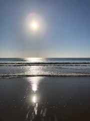 A serene beach scene with crystal-clear blue water, soft white sand, and a bright yellow sun shining overhead.