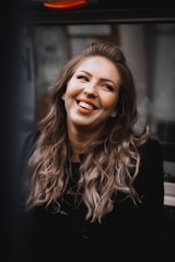 A joyful woman with natural curls wearing a stylish blackhairwigs wig, smiling confidently in a sunlit room.