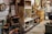 A cluttered antique store or flea market display with various vintage items on shelves and tables. There are old bottles, a fan, books, decorative plates, vintage signs, and a duck figurine. The setting is a dimly lit room with multiple wooden and metal shelving units filled with collectables and artifacts, giving a rustic and nostalgic feel.