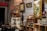 A room filled with an eclectic collection of vintage and retro items. Various framed artworks and memorabilia are displayed on the walls. A collection of small objects and antiques are arranged on shelves and cabinets, with decorative elements like glass bottles, figurines, and a lamp. The ambiance is nostalgic, evoking a sense of history and charm.