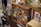 A variety of vintage and collectible items are displayed on wood shelves. There are several metal tins, boxes, old toy cars, and assorted memorabilia. The cabinet appears to be in a room with other collectibles, including a rustic metal container and framed artwork.