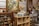 A vintage store display features a mix of old-fashioned objects and collectibles. There is a large framed painting of a scenic landscape, several collectible glasses in various colors on wooden shelves, and a variety of items such as vintage signs, mirrors, and decorative plates. Shelves are filled with retro memorabilia, including tins, books, and small model cars. The setting has a rustic and nostalgic atmosphere, with a mix of metal and wood materials.