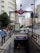 A city street features a subway entrance marked with a red and blue sign for 'Metro Santo Domingo'. The surrounding area includes tall buildings, visible traffic, and pedestrians. The skyline shows overcast skies with modern and historical architecture in the background.
