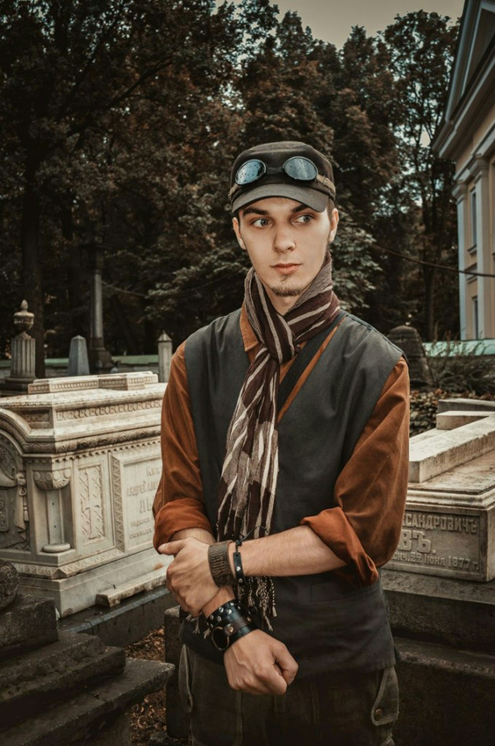 a man in a hat and scarf standing in front of a grave