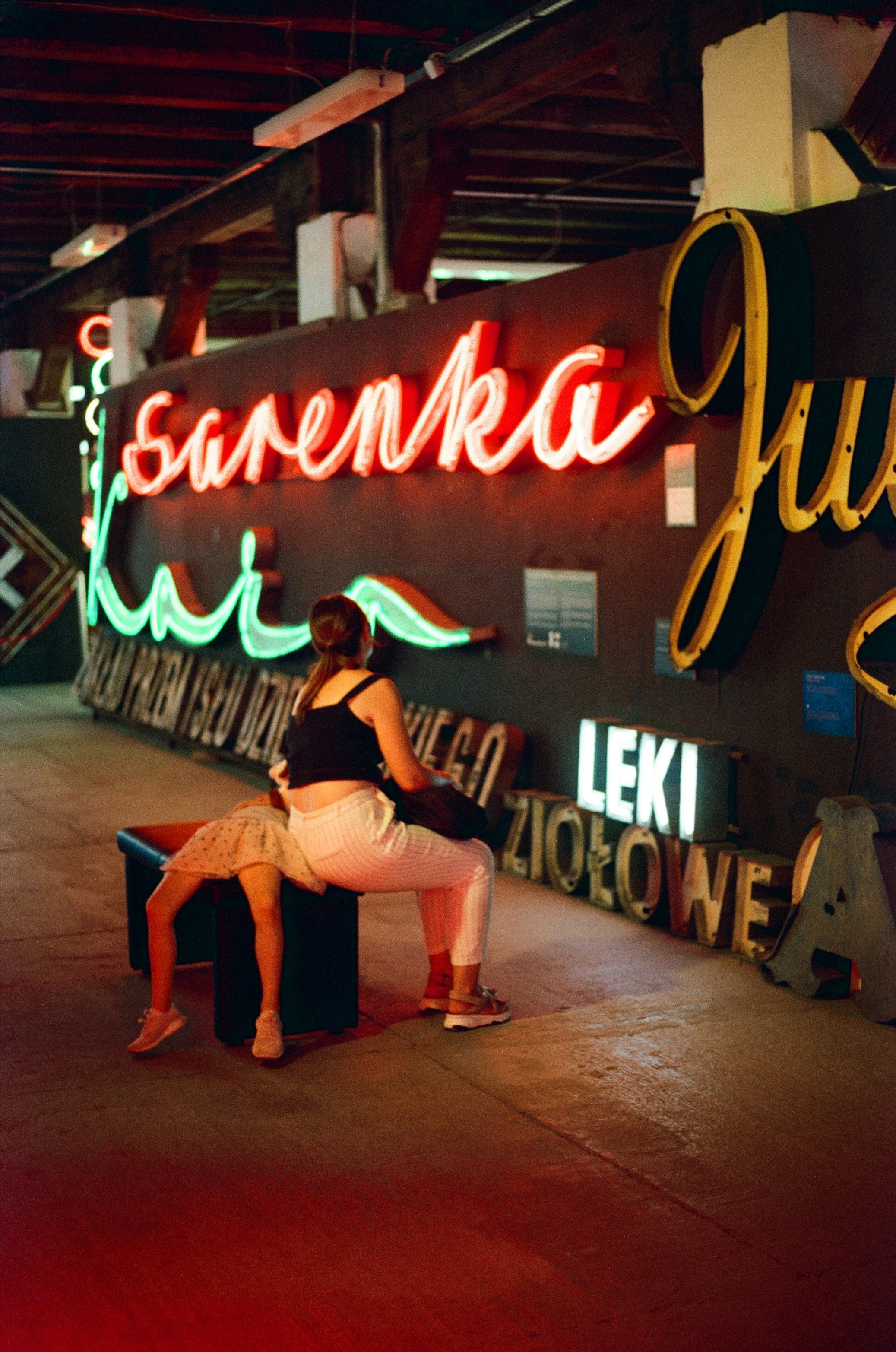 a woman sitting on a bench in front of a neon sign