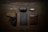 A neatly arranged flat lay of everyday carry items on a wooden surface. It includes a folding knife, a case labeled 'Bose', a car key fob, a firearm in a holster, a pen, a closed notebook, and a brown leather wallet.