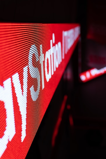 A close-up view of an LED display featuring bright red and white text. The text is prominently visible with a strong diagonal perspective, creating a dynamic visual effect. The background is blurred, emphasizing the sharpness of the LED lights.