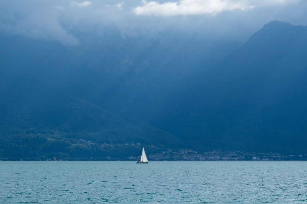 una barca a vela in un grande specchio d'acqua con montagne sullo sfondo