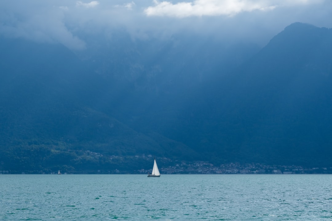 a sailboat in a large body of water with mountains in the background, Harmony of nature