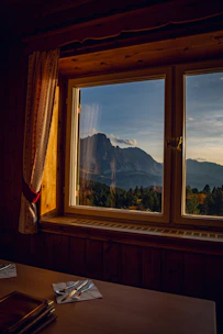 A cozy wooden kathkuni room bathed in warm sunlight with mountain views through the window.