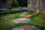 A lush green lawn with stone pathways and decorative lighting at dusk.