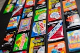A collection of various vintage baseball card packs arranged on a dark surface. The packs feature vibrant and colorful designs with bold text, representing different brands and styles of baseball cards from past decades.