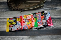 A collection of vintage baseball card packs, arranged in a row, displayed on a wooden surface with a baseball glove partially visible in the background.