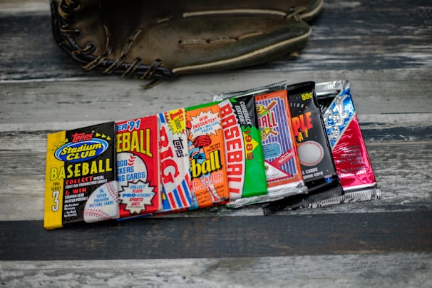 A collection of vintage baseball card packs, arranged in a row, displayed on a wooden surface with a baseball glove partially visible in the background.