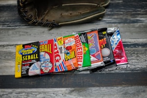 A collection of vintage baseball card packs, arranged in a row, displayed on a wooden surface with a baseball glove partially visible in the background.