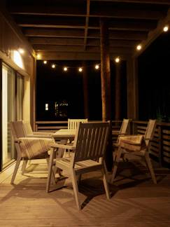 A cozy outdoor bar table set with warm string lights overhead on a wooden deck.