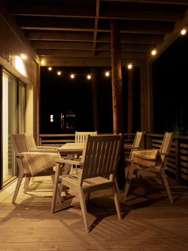 A cozy outdoor patio featuring a rattan dining chair set under soft string lights at dusk.