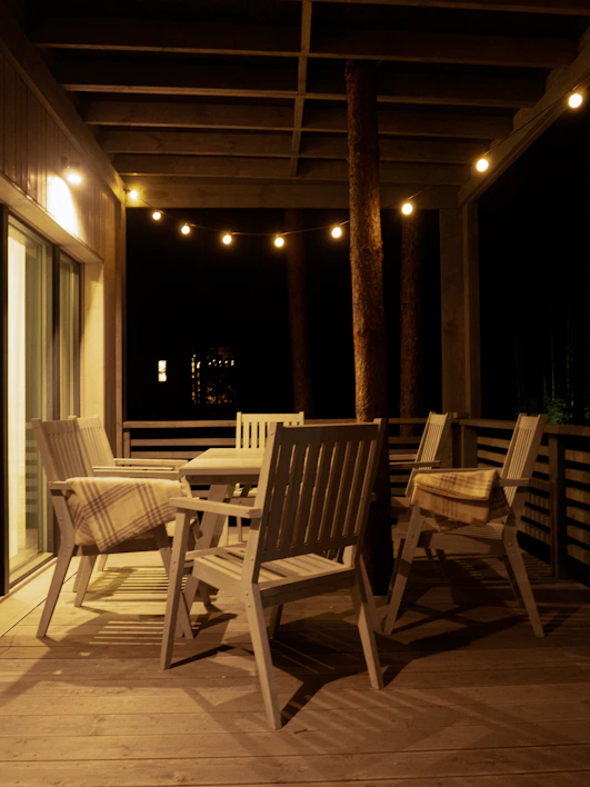 A cozy outdoor bar table set with warm string lights overhead on a wooden deck.