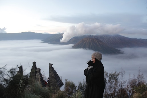 a woman standing on top of a mountain looking at the clouds