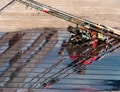 Several fishing rods are resting on a wet wooden surface, with reflections from the water creating interesting patterns. The rods are equipped with different colored reels.