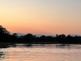 A calm lake reflecting the soft colors of a sunset sky surrounded by trees.