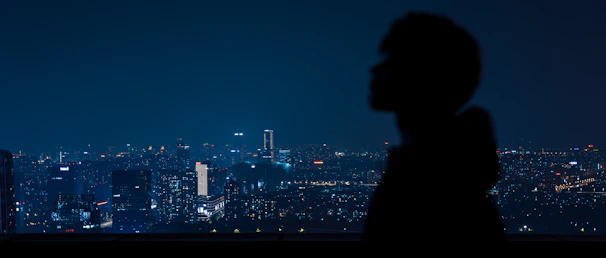 A dramatic nighttime cityscape with a lone figure silhouetted against glowing streetlights, evoking mystery and depth.
