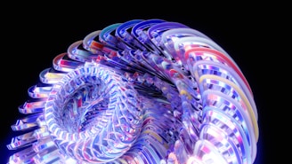 A complex, swirling 3D structure composed of intertwining, colorful ribbons that create a dynamic and futuristic appearance. The ribbons are glossy and reflective, showcasing a spectrum of vibrant colors against a black background.