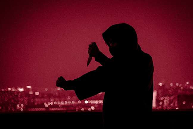 A shadowy figure holding a spy gadget against a backdrop of black and silver decor.