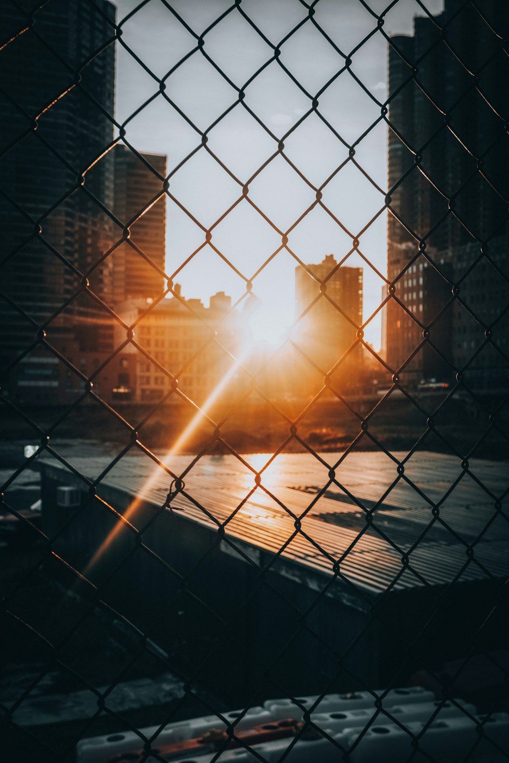 the sun is setting behind a chain link fence