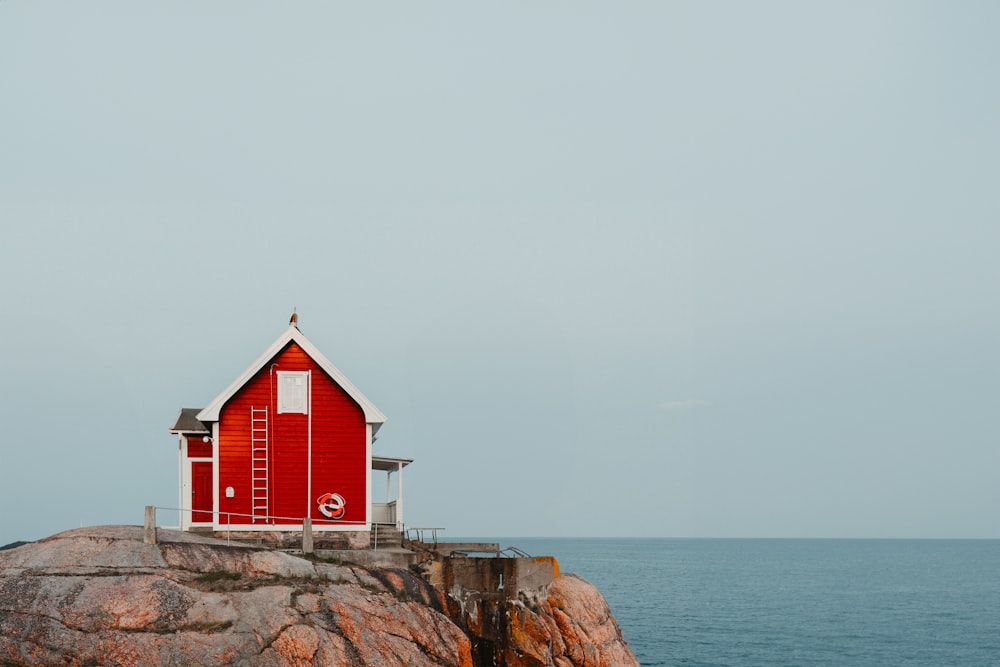 a red house sitting on top of a rock next to the ocean