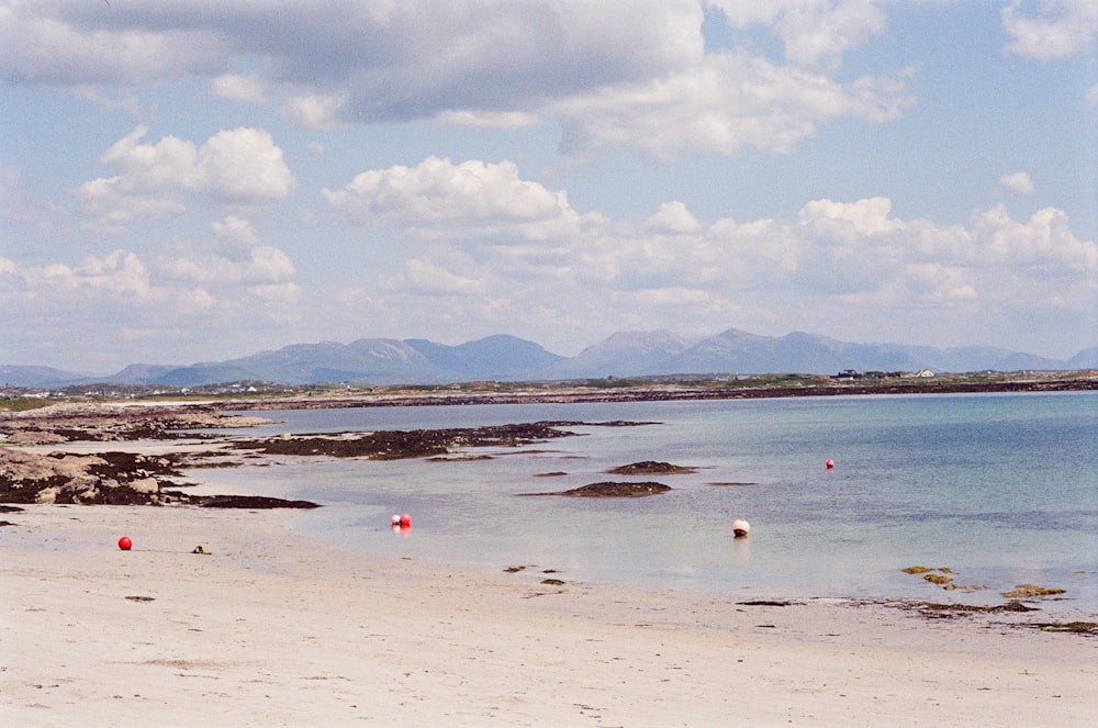 a sandy beach with a body of water and mountains in the background