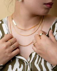 Close-up of a young woman wearing layered minimalist silver necklaces and bold rings in an urban setting.
