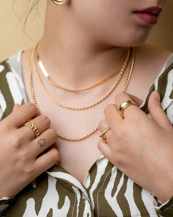 Close-up of a young woman wearing layered minimalist silver necklaces and bold rings in an urban setting.