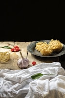 A rustic wooden table with ingredients for a pasta recipe: tomatoes, garlic, and basil.