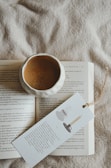 A cuddle cup mug resting on a wooden table next to an open book and soft blanket.
