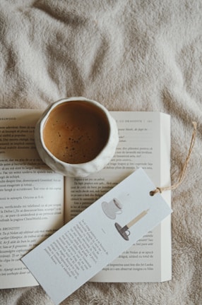 A cuddle cup mug resting on a wooden table next to an open book and soft blanket.