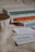 A cozy scene features a ceramic mug, a stack of books with colorful spines, and two cards on a soft, beige surface. The books have decorative covers with titles visible on the spines, and the cards are part of a game, with one card prominently displaying 'The Hygge Game.'