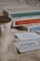 A cozy scene features a ceramic mug, a stack of books with colorful spines, and two cards on a soft, beige surface. The books have decorative covers with titles visible on the spines, and the cards are part of a game, with one card prominently displaying 'The Hygge Game.'