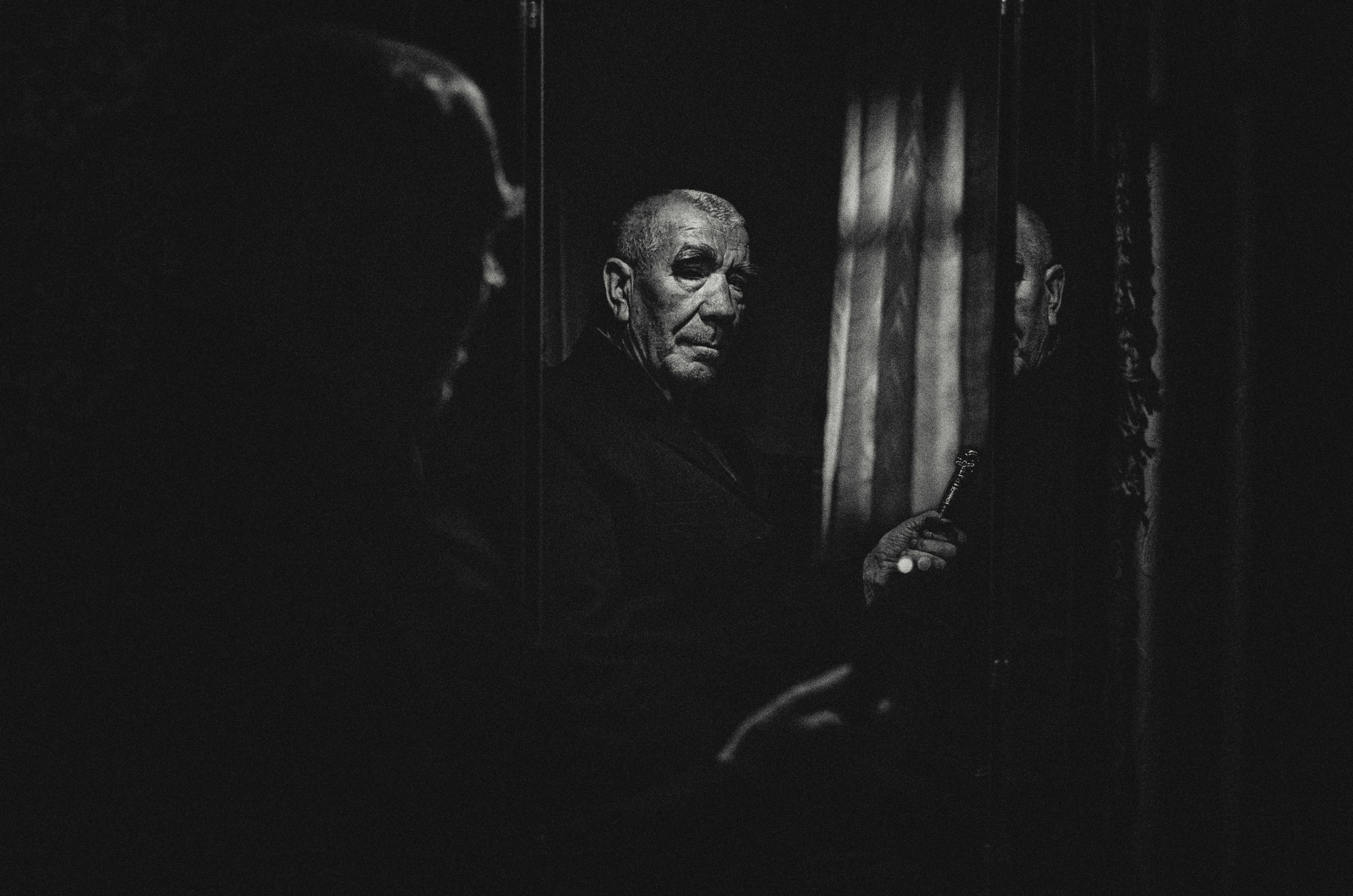 A person's face is reflected infinitely in a series of mirrors, creating a disorienting echo chamber effect in a dark, moody setting.