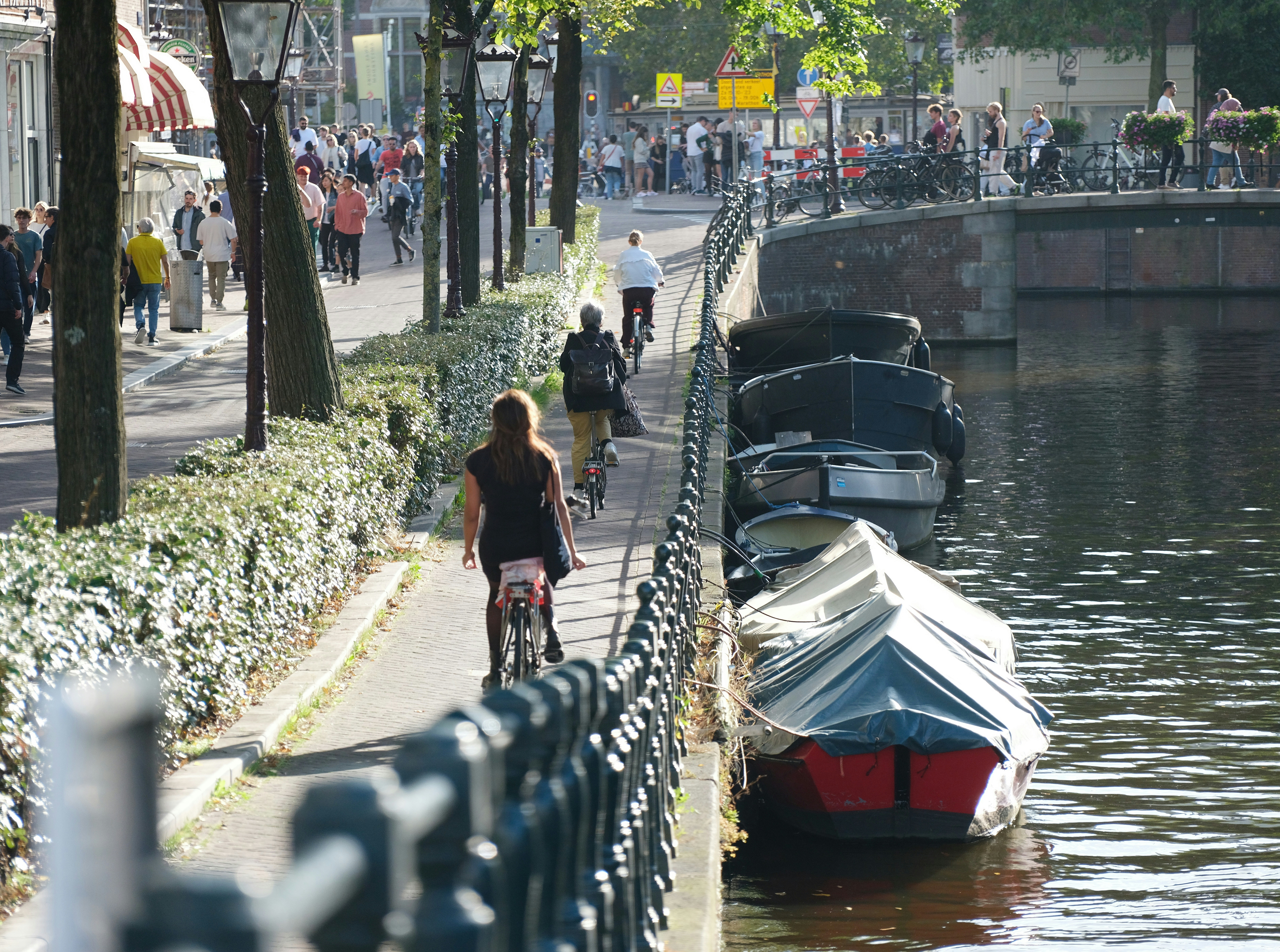 a woman riding a bike next to a body of water, Amsterdam, bikes, and channels