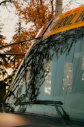 A shiny, clean school bus parked in front of a Maryland school building with autumn leaves around.