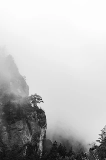 A misty evening scene capturing solitary cliffs shrouded in fog with muted tones and delicate textures.