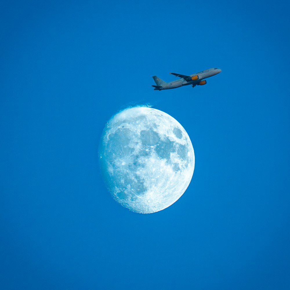 an airplane flying over the moon in a clear blue sky