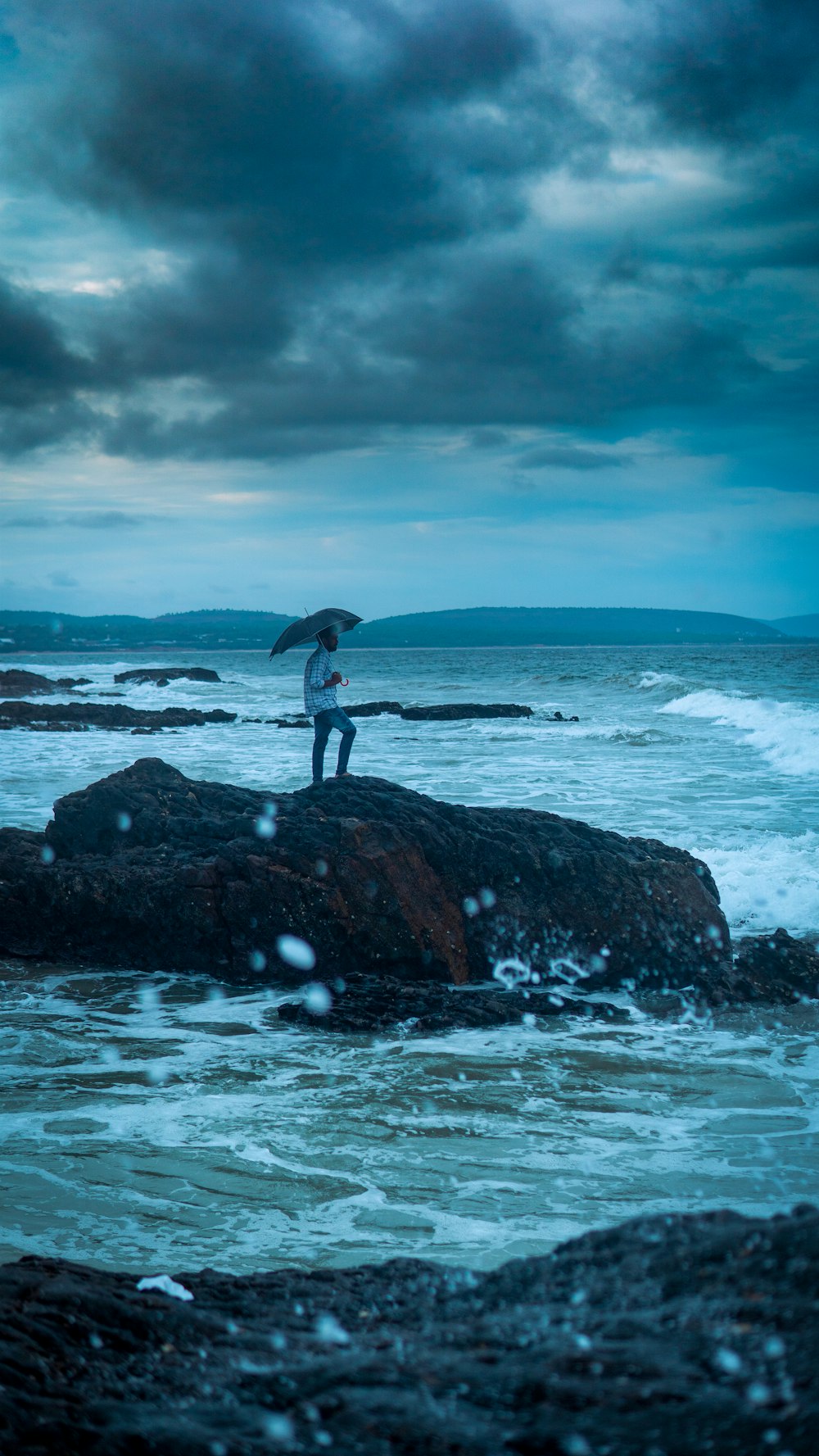 a person standing on a rock with an umbrella
