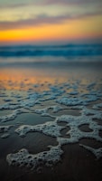 Soft ocean foam washing over a sandy beach at sunset.