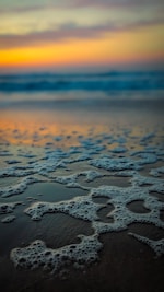 Soft ocean foam washing over a sandy beach at sunset.