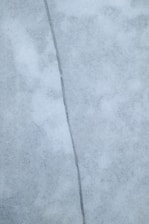 A close-up view of a surface with a noticeable crack running vertically through the center. The surface appears to be made of a smooth, marble-like material with a light gray color and subtle texture variations.