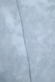 A close-up view of a surface with a noticeable crack running vertically through the center. The surface appears to be made of a smooth, marble-like material with a light gray color and subtle texture variations.