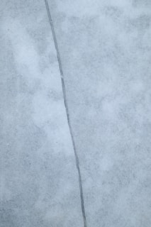 A close-up view of a surface with a noticeable crack running vertically through the center. The surface appears to be made of a smooth, marble-like material with a light gray color and subtle texture variations.